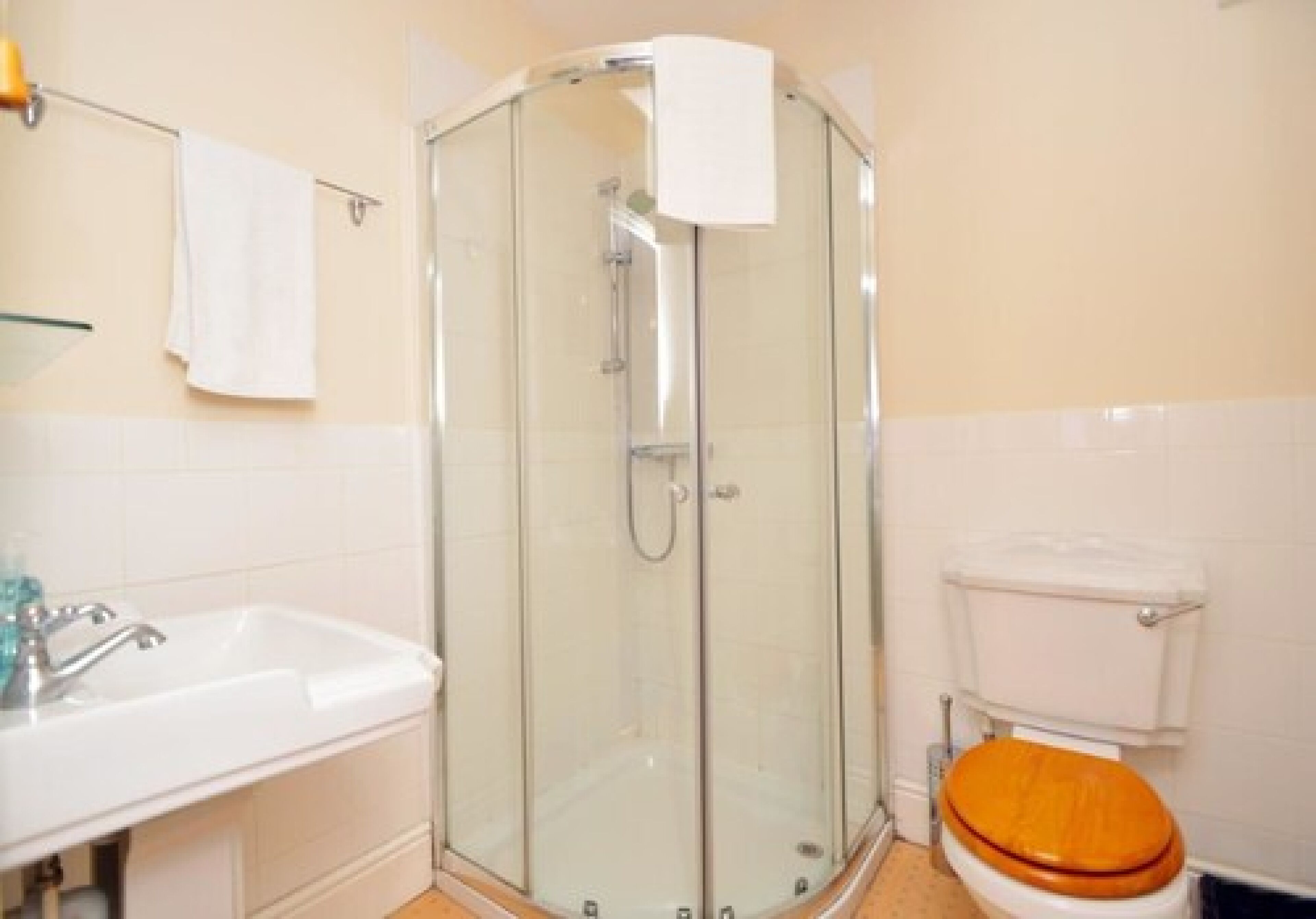 A bathroom with a glass-enclosed shower, a white sink, and a toilet with an orange seat.