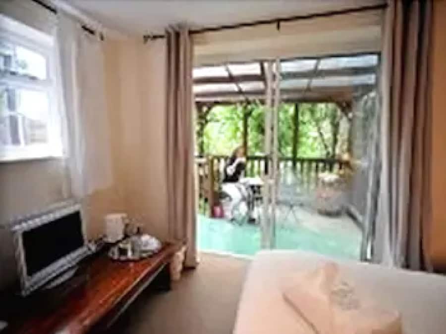 A hotel room with a TV, a desk, and a balcony with a view of the outdoors.