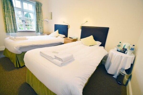 A hotel room with two single beds, a small table with toiletries, and a window with curtains.