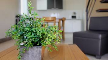 Uma planta em vaso sobre uma mesa de madeira em um cômodo com uma sala de jantar e uma cozinha ao fundo.