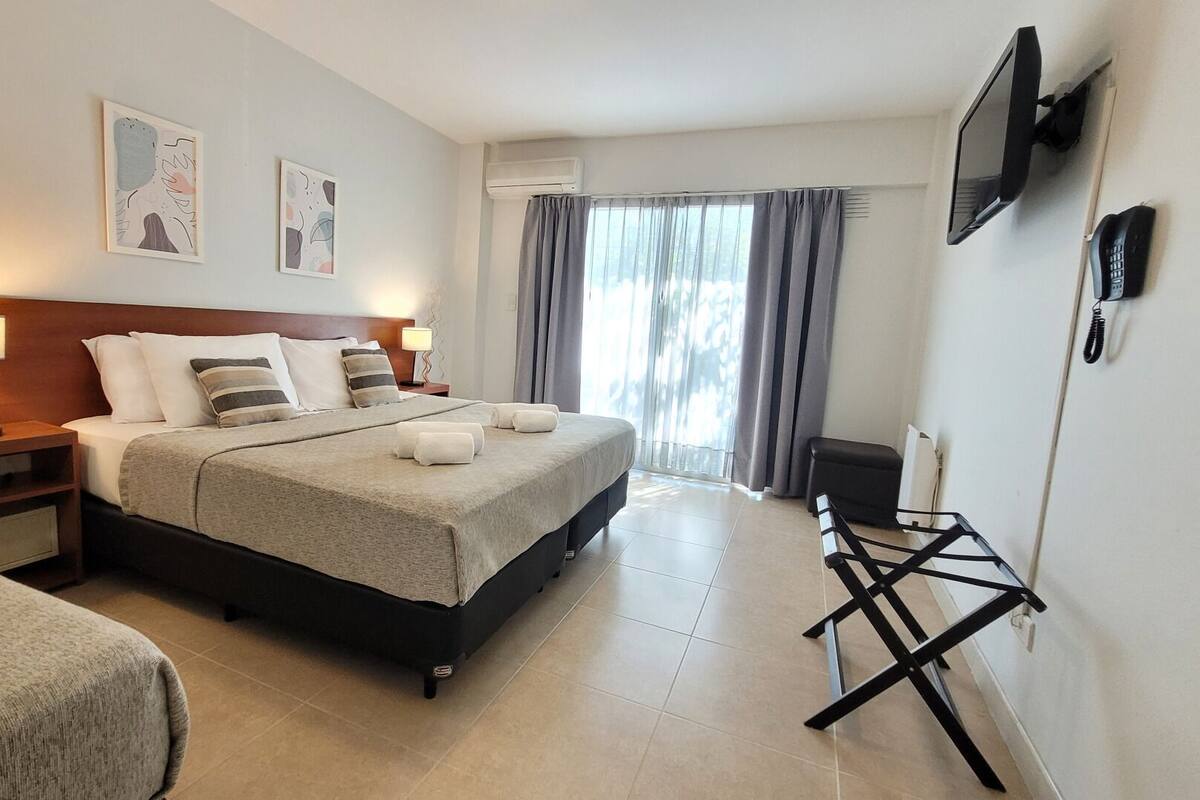 Habitación de hotel con cama, mesitas de noche, televisión y ventana con cortinas.