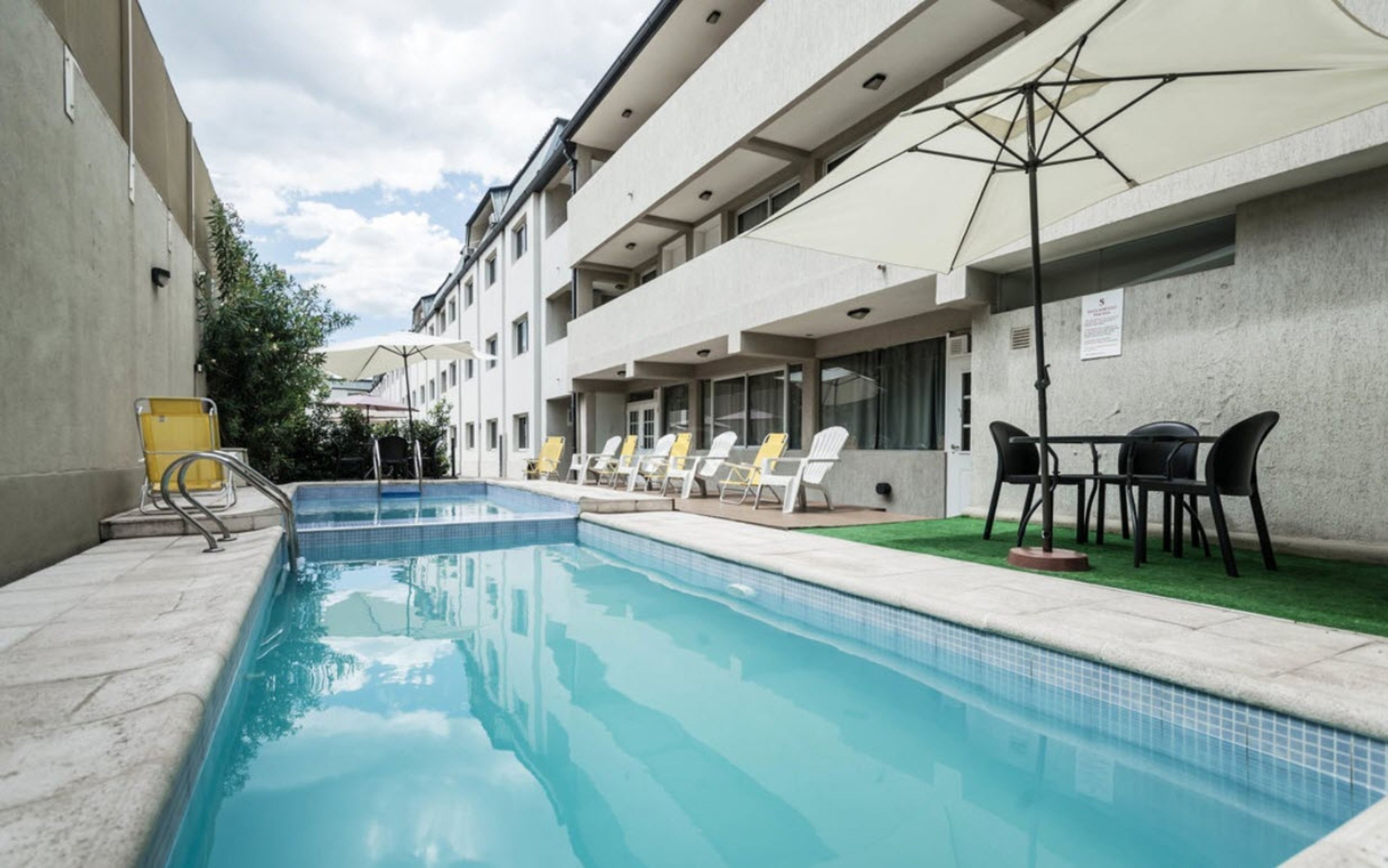 Ein Swimmingpool mit Liegestühlen und Sonnenschirmen, umgeben von einem Gebäude mit mehreren Balkonen.