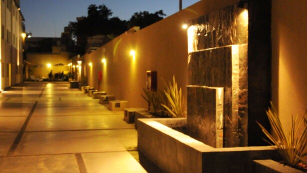 Un couloir nocturne agrémenté de bancs, d’un élément décoratif aquatique et d’un mur en pierre.