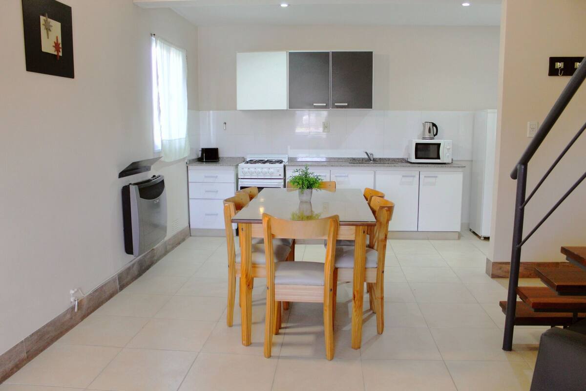 Una cocina moderna con armarios blancos, una mesa de comedor con sillas, un microondas y una estufa a gas.