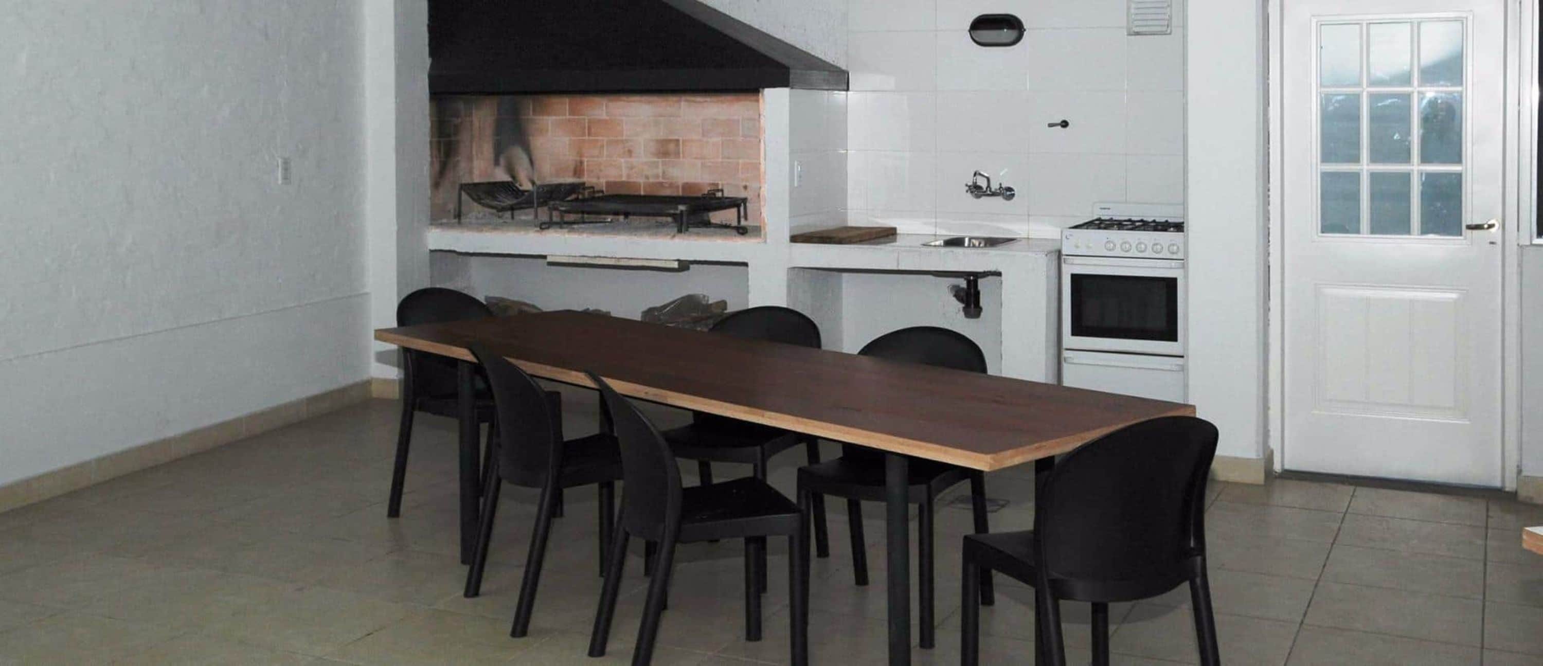 A compact kitchen with a long wooden table and black chairs, a built-in oven, and a brick oven.