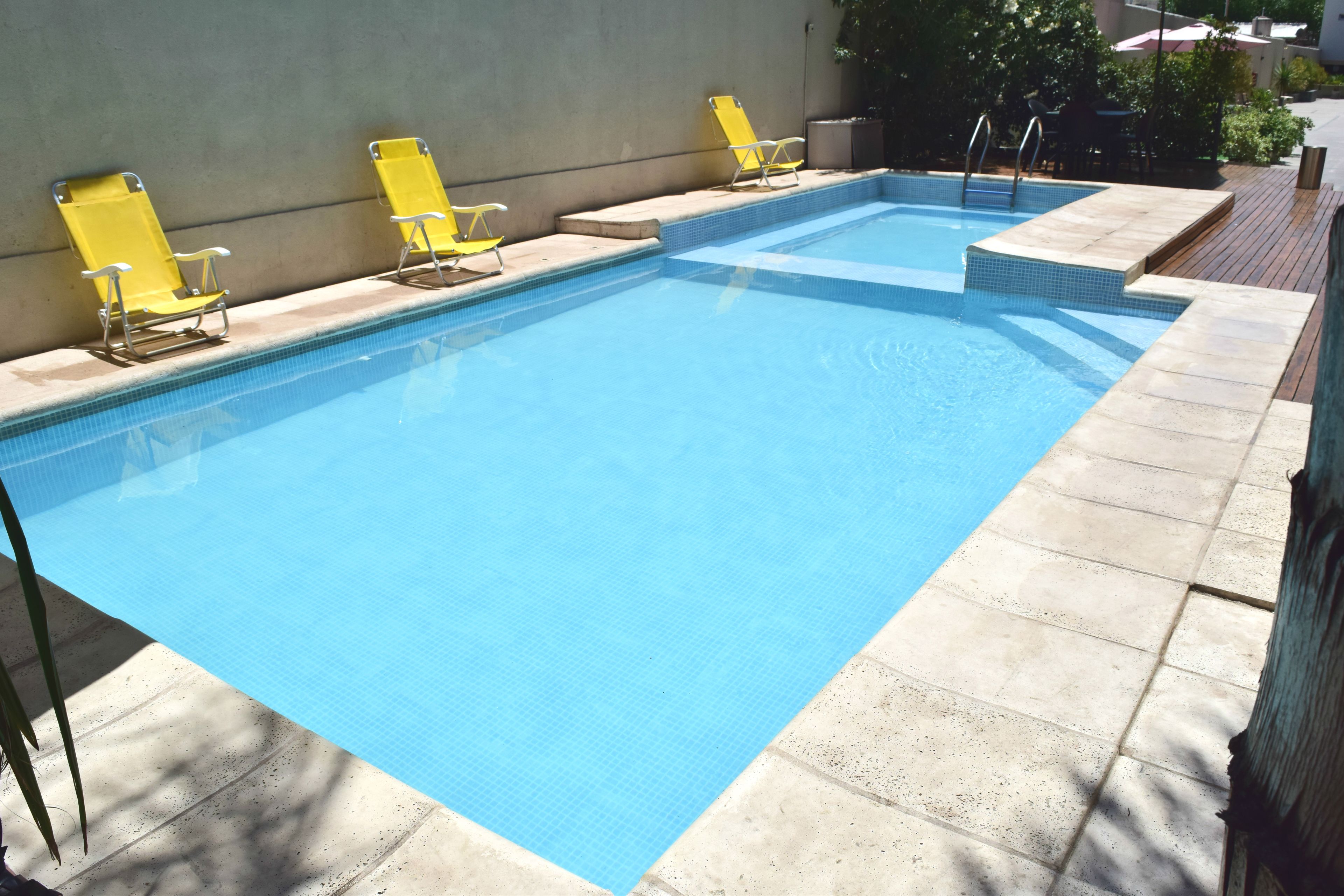 Ein rechteckiger Swimmingpool mit klarem, blauem Wasser, umgeben von einer Fliesenveranda und gelben Liegestühlen.