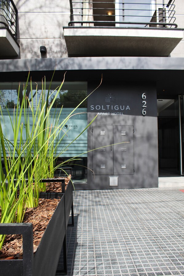 A modern building with a sign reading "Soltigua Apart Hotel" and a metal gate with a keycard reader.
