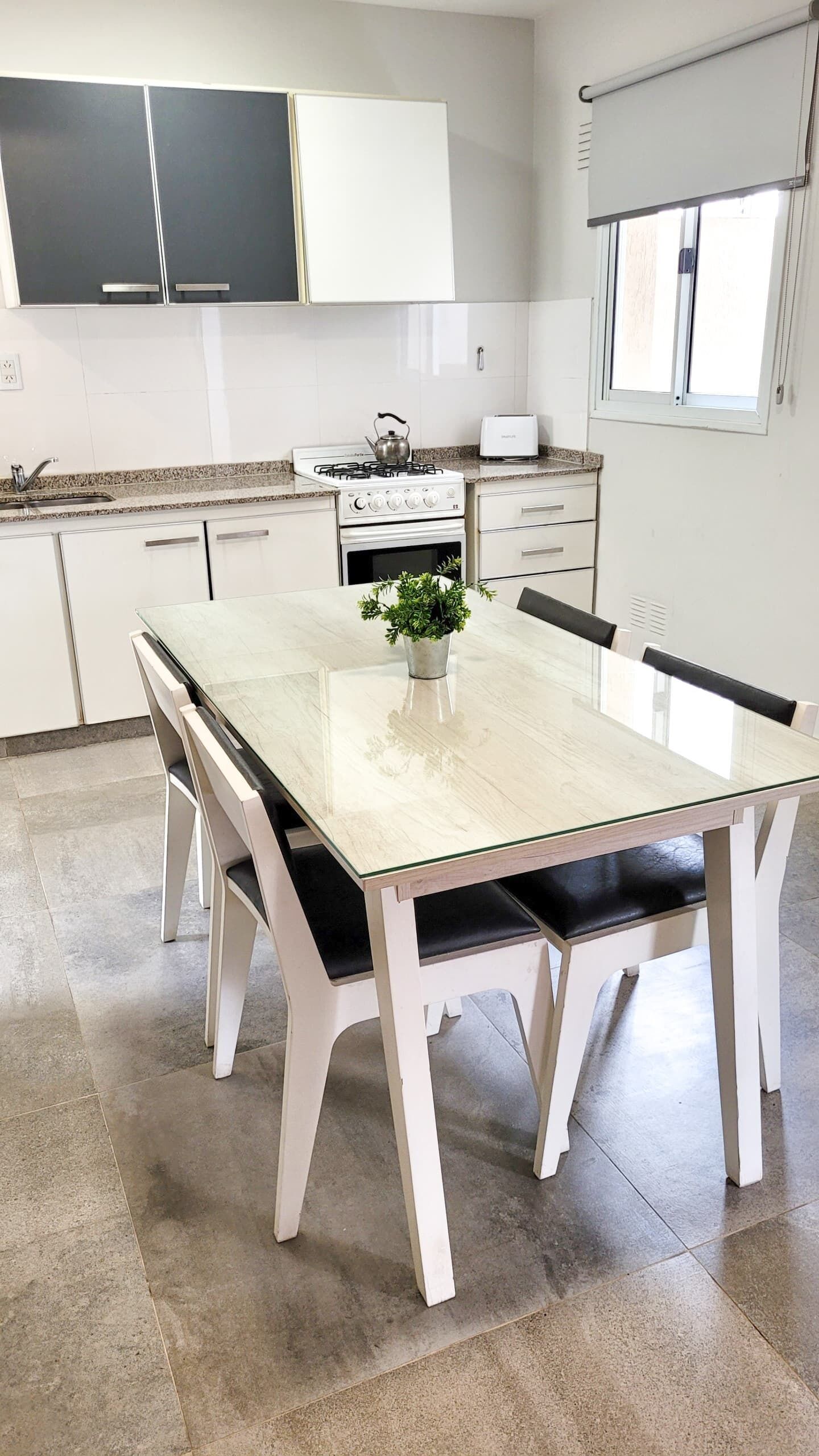 Una cocina moderna con armarios blancos, estufa a gas, tostadora y una mesa de comedor con sillas.