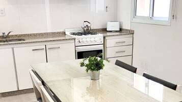 Una cocina moderna con armarios blancos, estufa a gas, tostadora y una mesa de comedor con sillas.