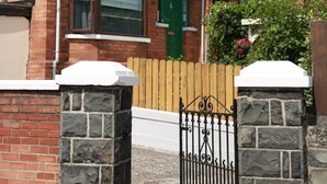 A two-story brick house with a green door, a stone wall, and a metal gate. - Greenmount Bed & Breakfast (Belfast)