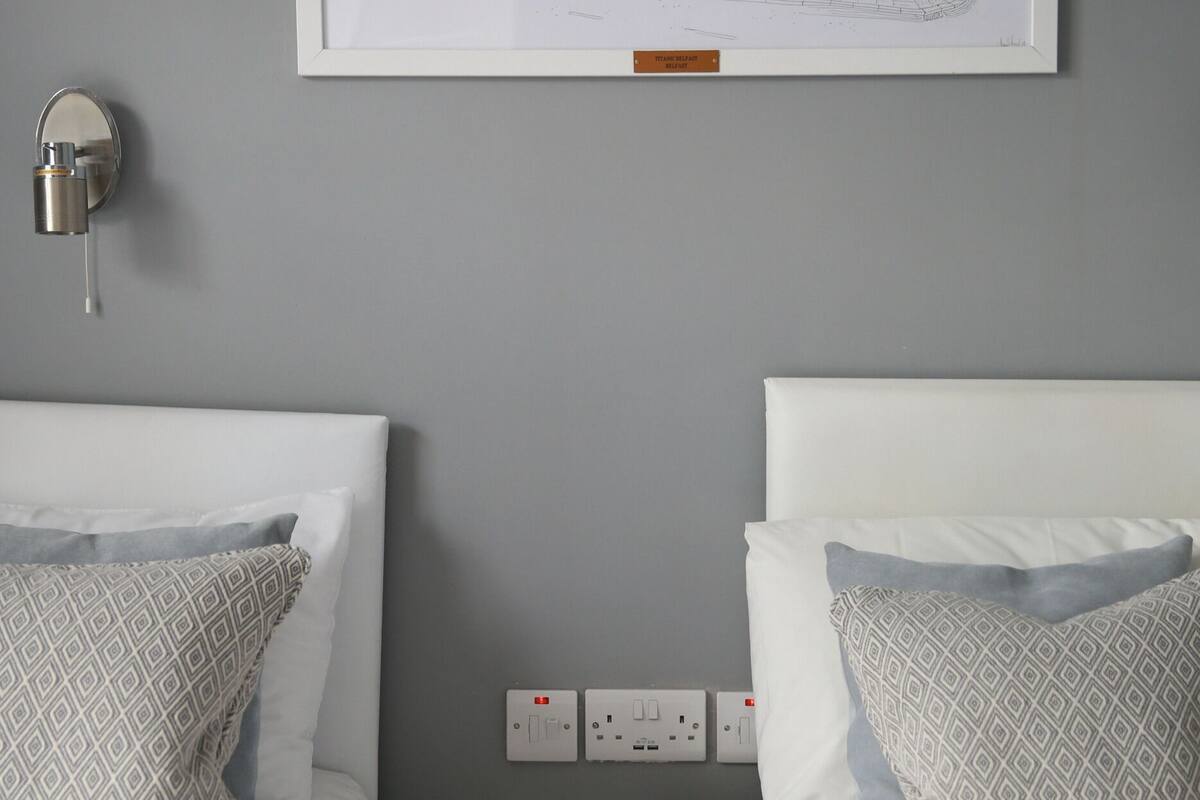A bedroom with two beds, a framed architectural sketch on the wall, a bedside lamp, and a decorative object on the nightstand.
