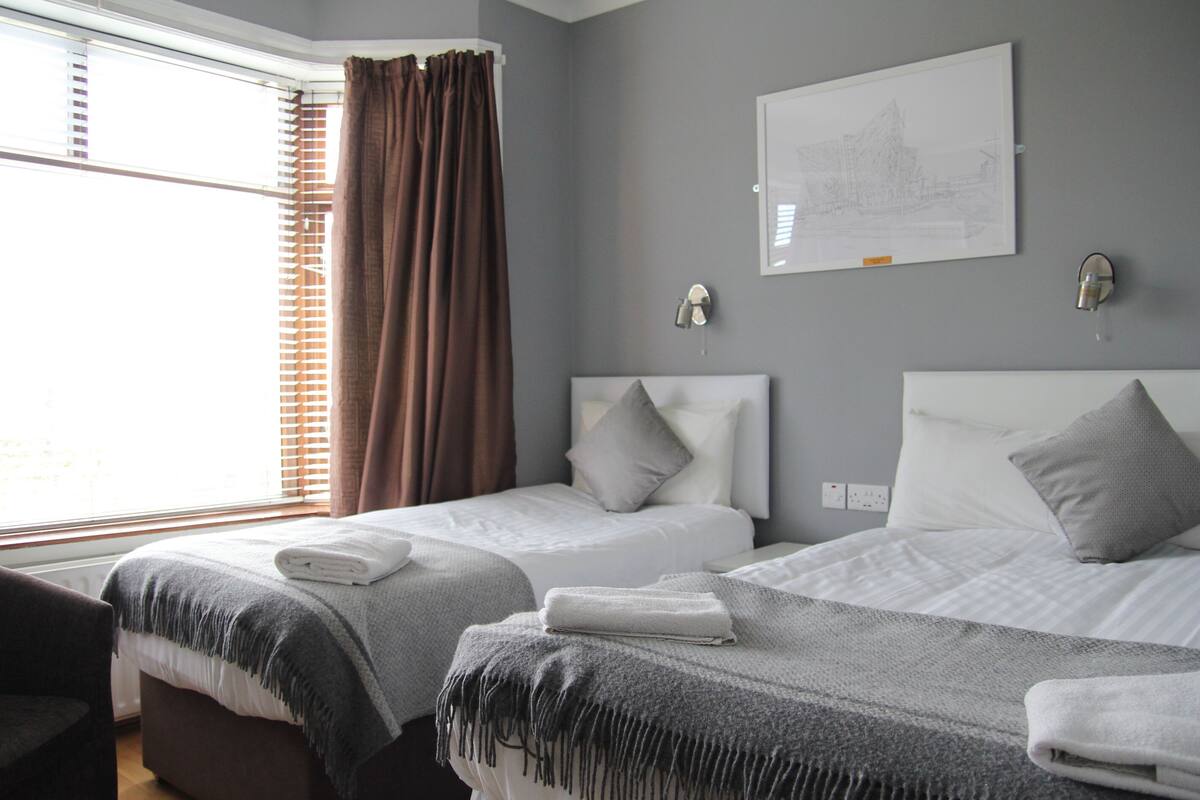 A hotel room with two beds, a window with blinds, a wall-mounted light, and a framed picture.