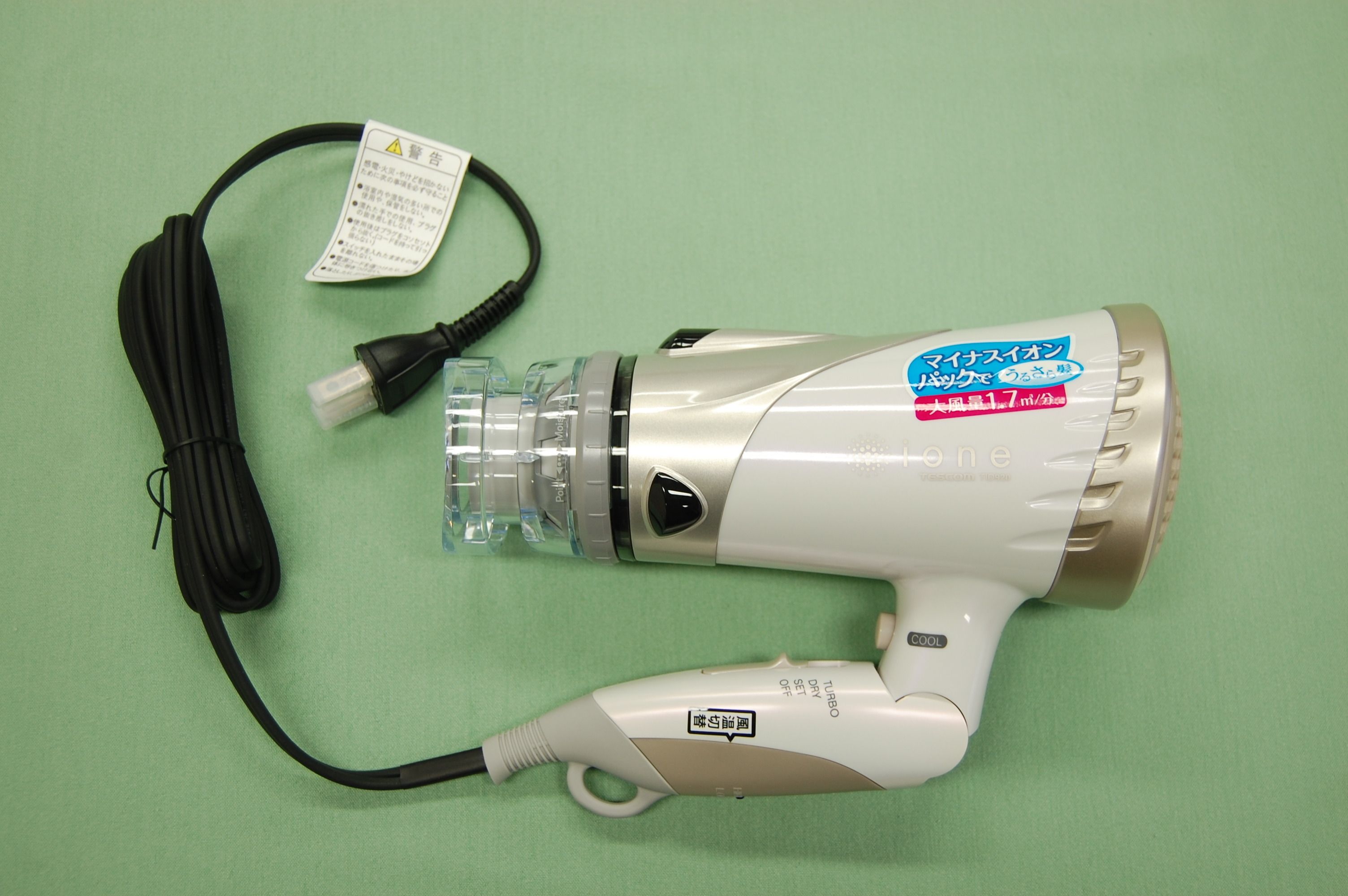 A portable hair dryer with a clear water bottle attached, a power cord, and a label with text.