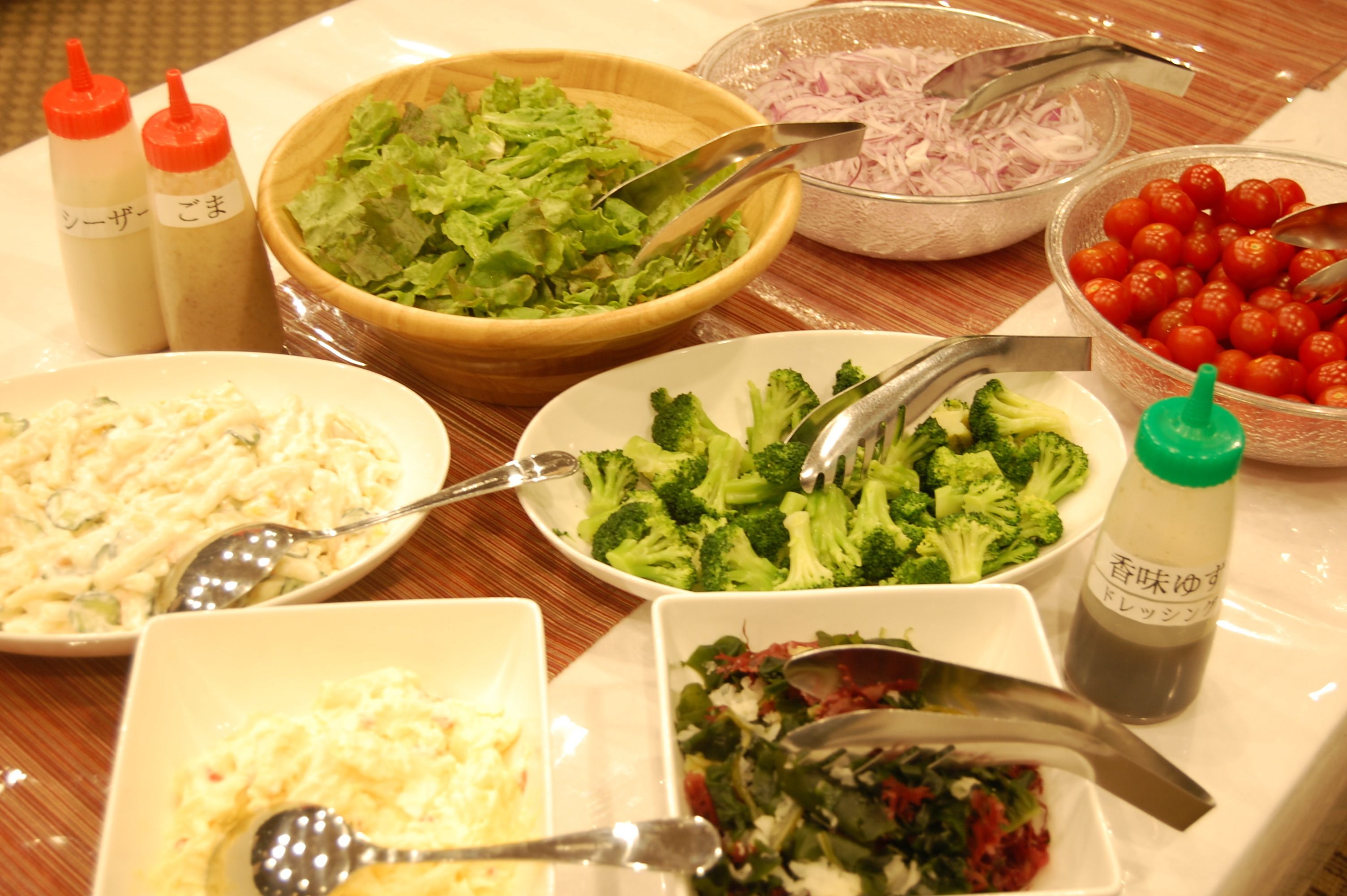 A table with various dishes including salads, broccoli, and a bowl of cherry tomatoes.