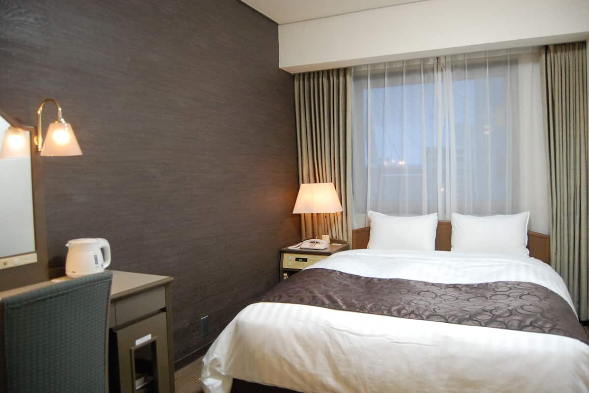 A hotel room with a bed, a desk with a lamp, a telephone, and a coffee maker.