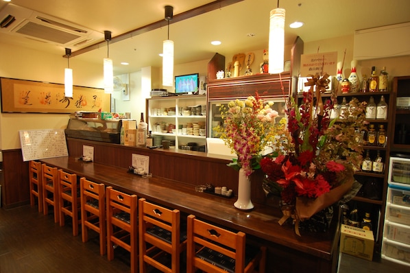 A restaurant interior with wooden chairs, a counter, a television, and a display of flowers.