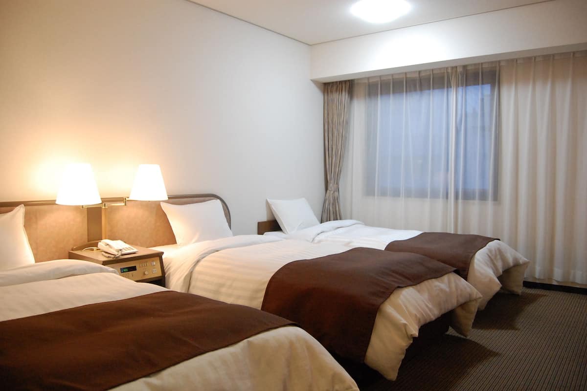A hotel room with two beds, a nightstand with a phone, and a window with curtains.