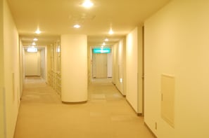 A long, narrow hallway with a series of doors on one side and a bright exit sign at the end.