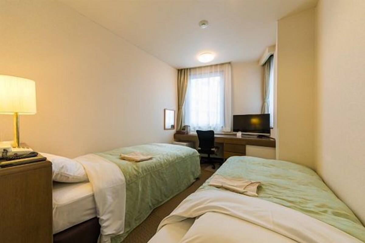 Een hotelkamer met twee bedden, een bureau, een stoel, een televisie en een lamp.