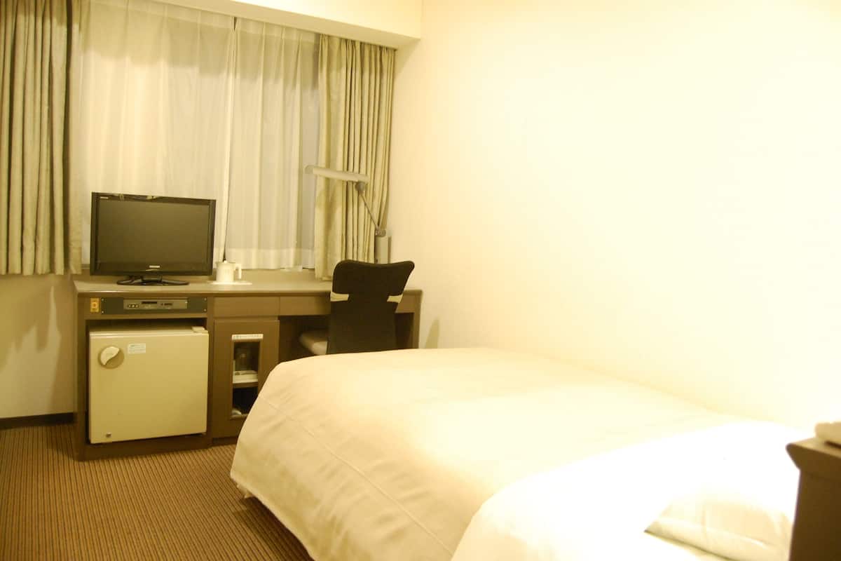 A hotel room with a bed, a desk with a computer, a chair, and a small refrigerator.