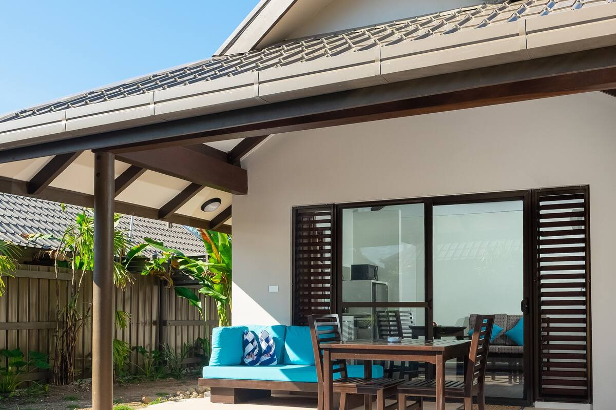 A poolside area with a covered seating area, a table, and chairs.