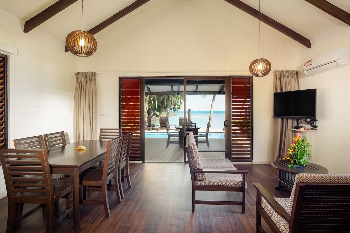 A dining area with wooden furniture, a TV, and a view of the ocean.