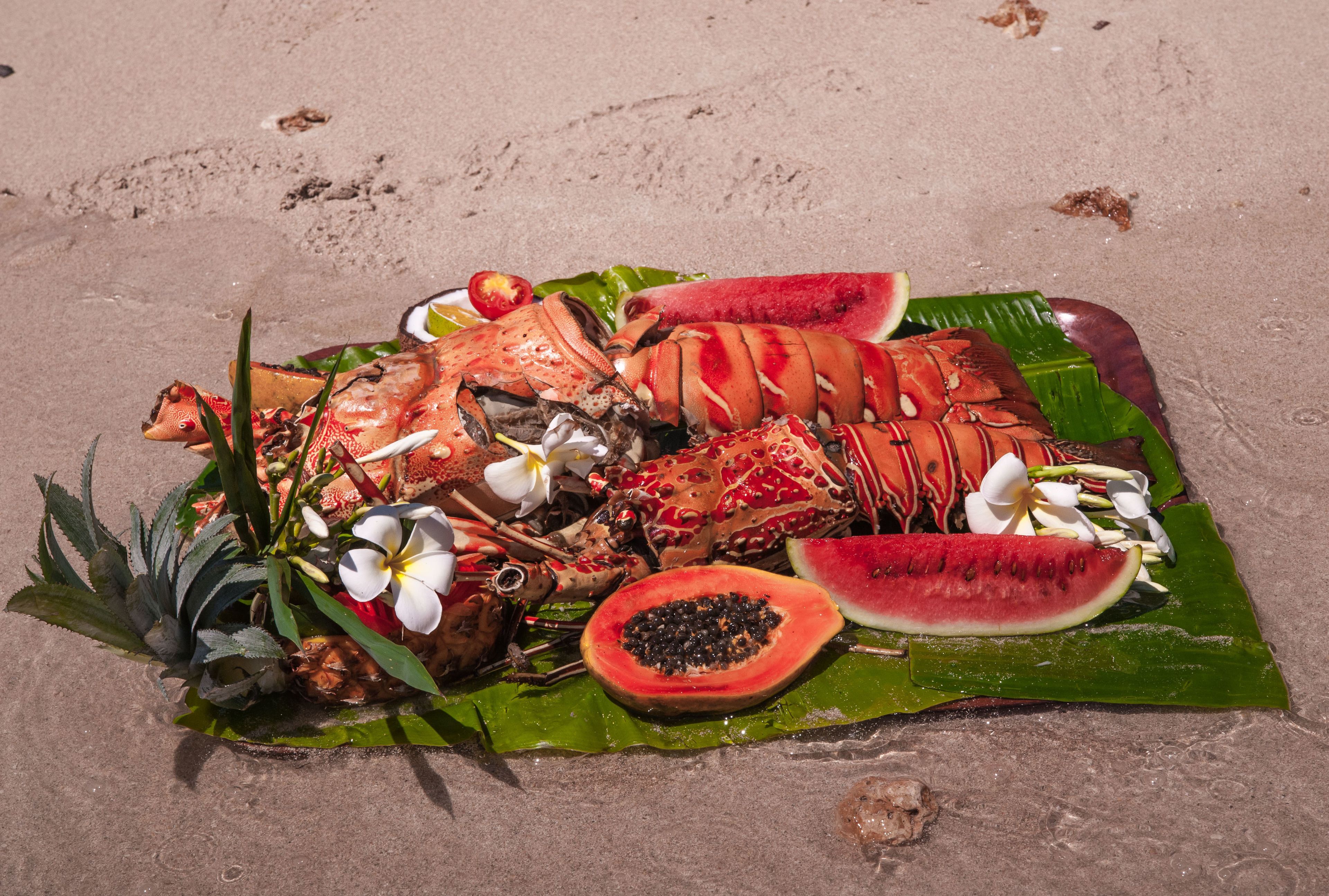 A tropical fruit and lobster platter on a banana leaf.