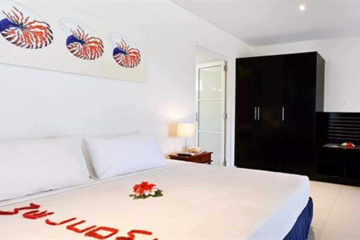 A hotel room with a large bed, a wardrobe, a desk with a lamp, and a wall with decorative shells.