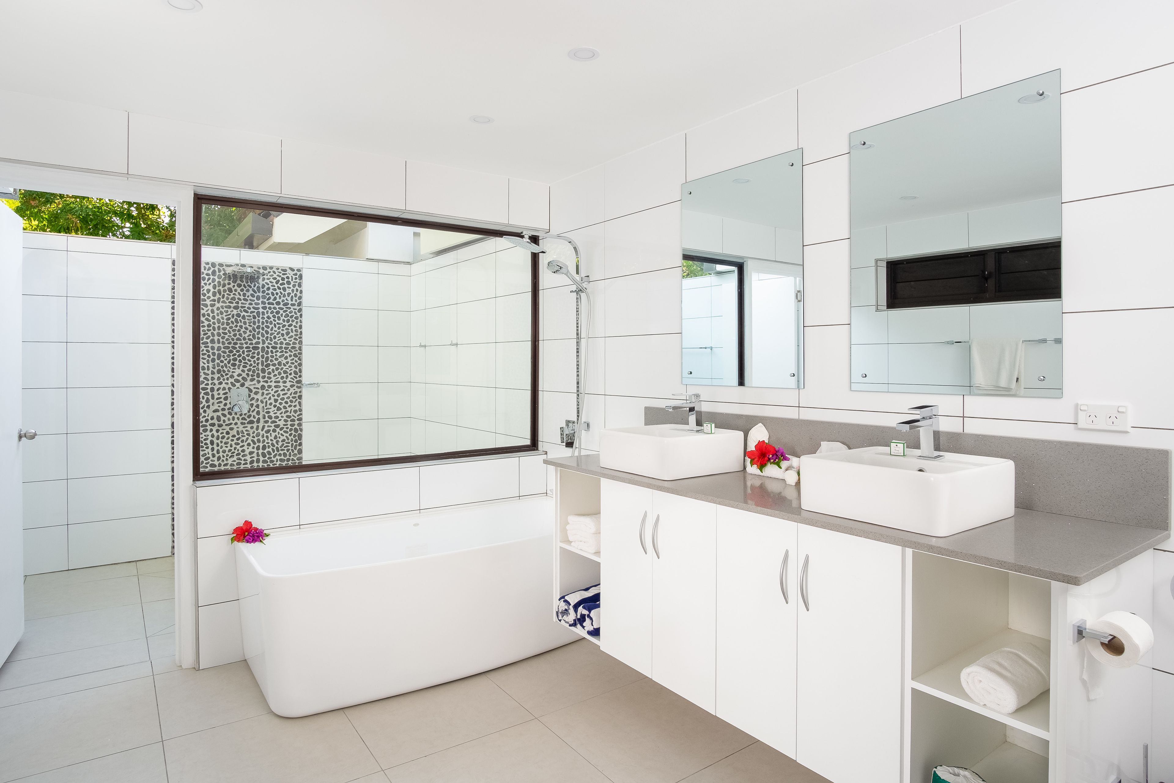 A modern bathroom with a large bathtub, two sinks, and a walk-in shower.