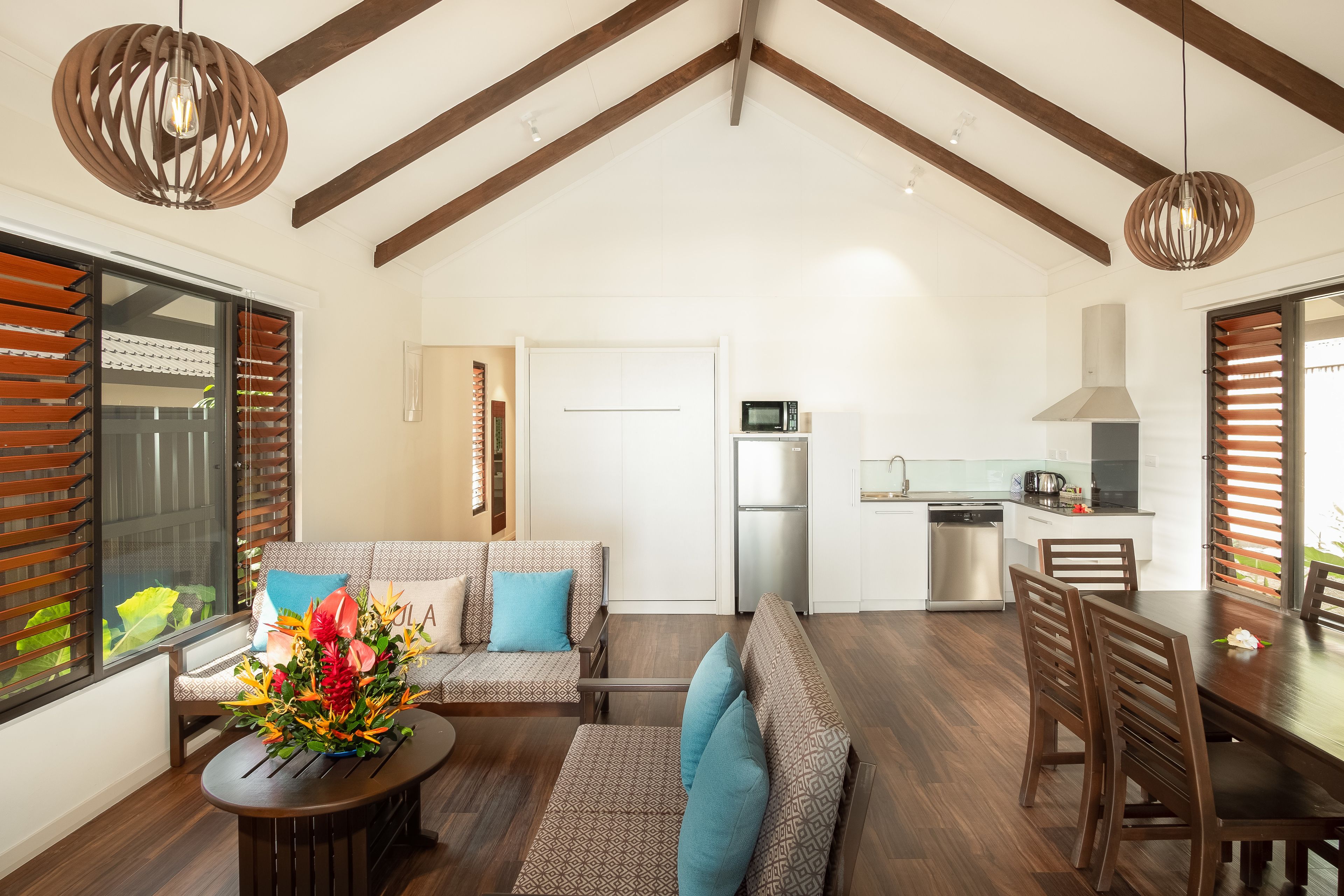 A spacious living area with a sofa set, dining table, and kitchen in the background.