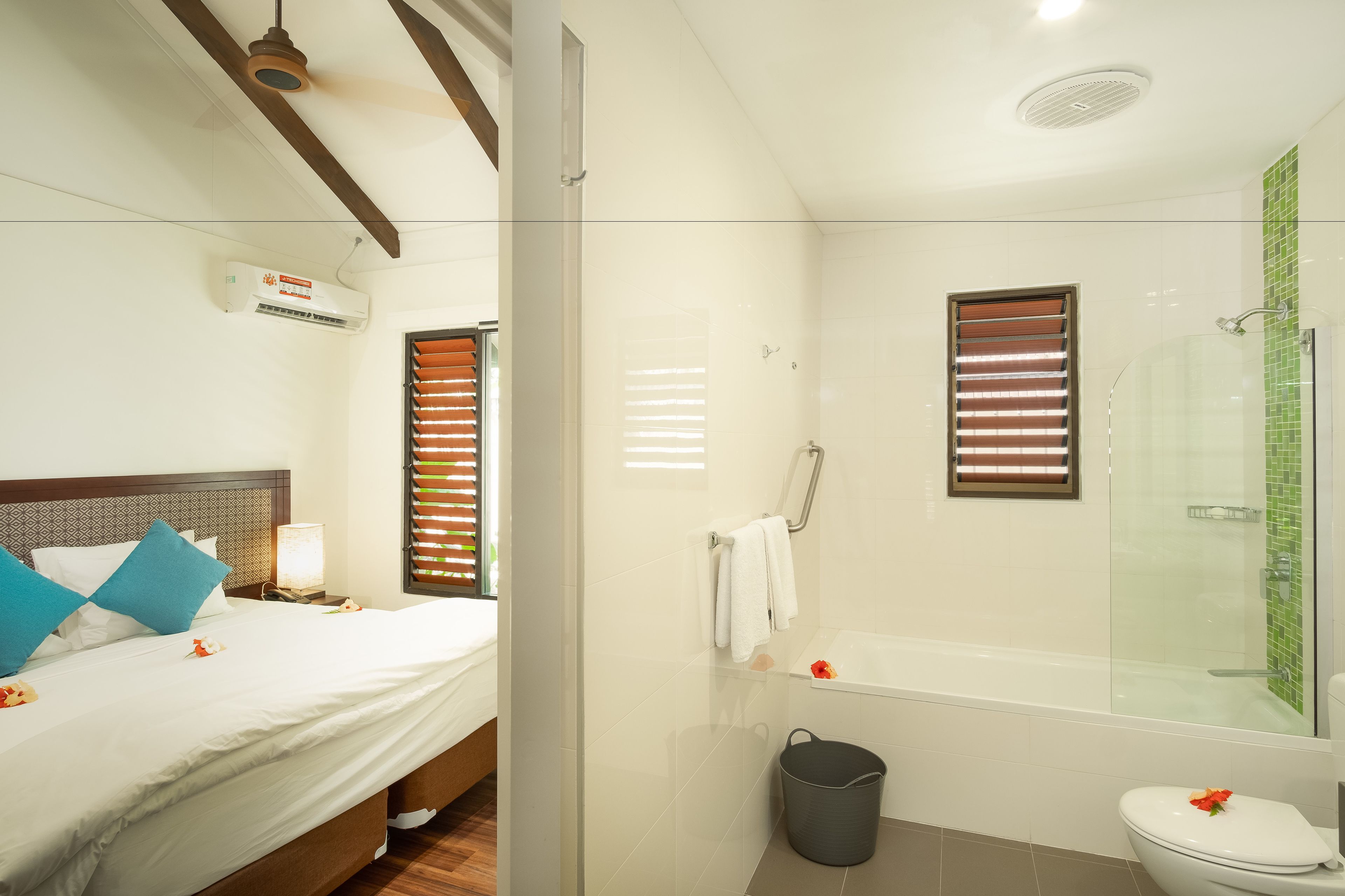 A hotel room with a bed, bedside table, lamp, and a bathroom with a shower, toilet, and bathtub.
