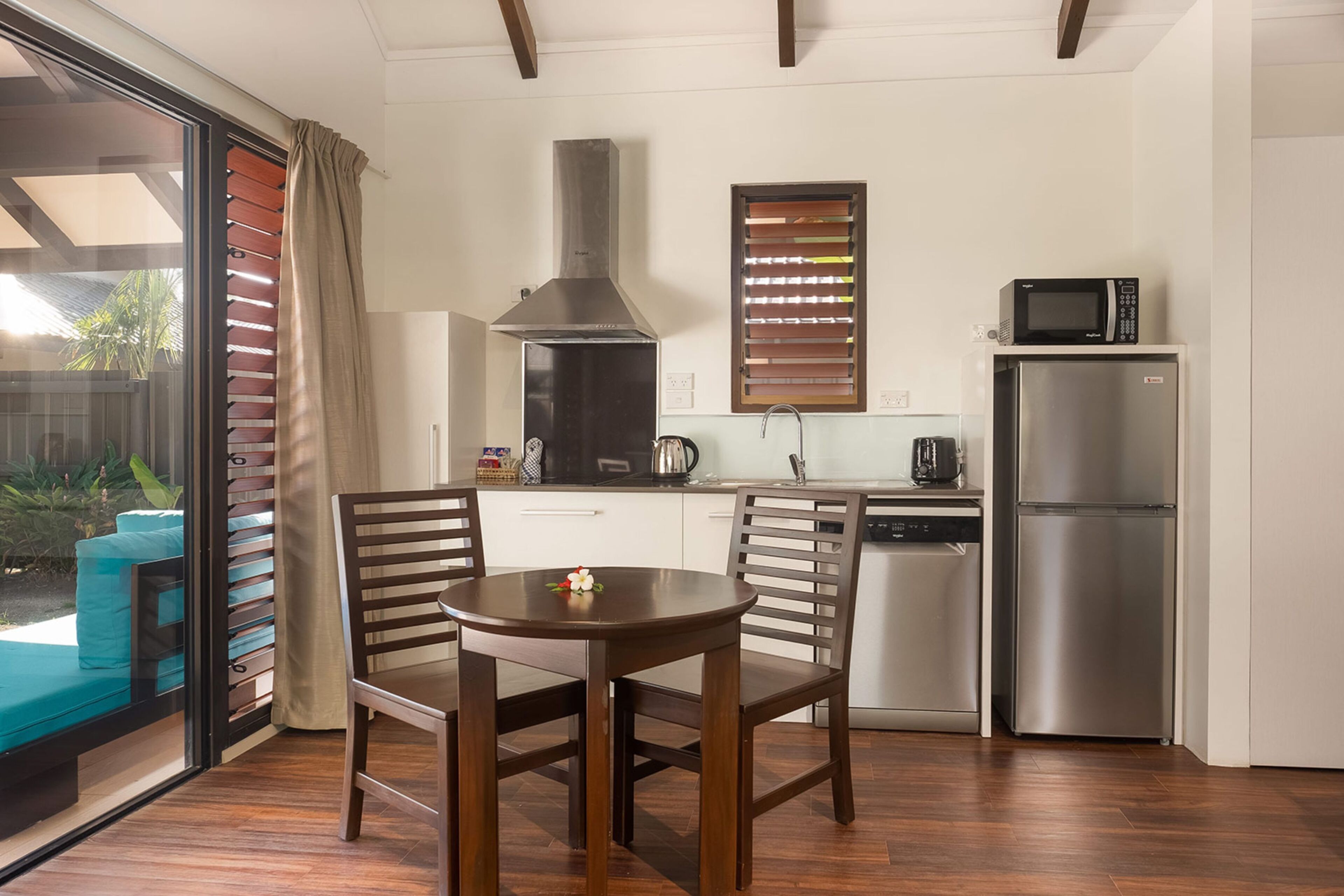 A compact kitchen with a dining area, a built-in microwave, a stainless steel refrigerator, and a sliding glass door leading to an outdoor area.