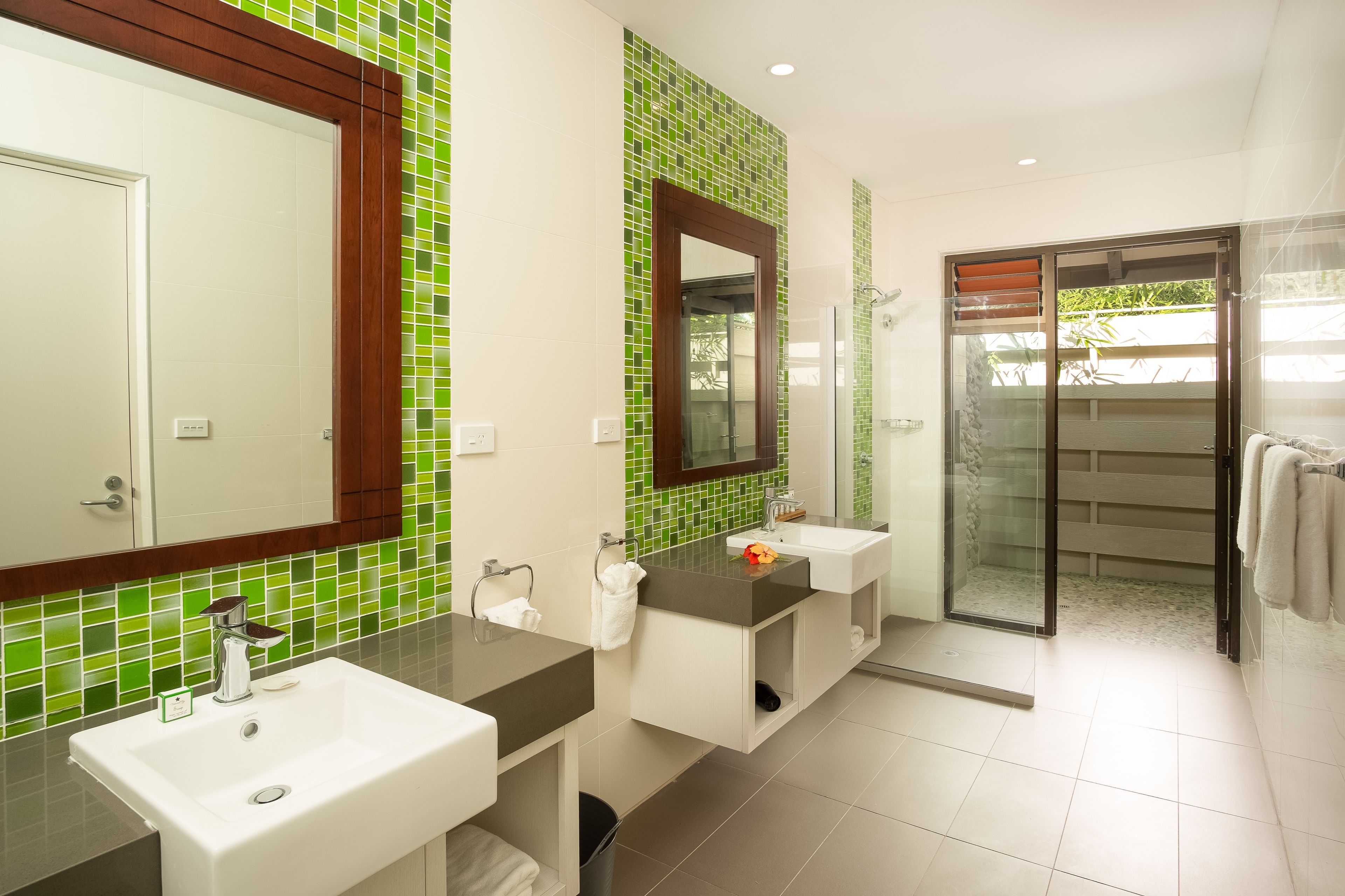 A modern bathroom with two sinks, a large mirror, and a glass shower enclosure.
