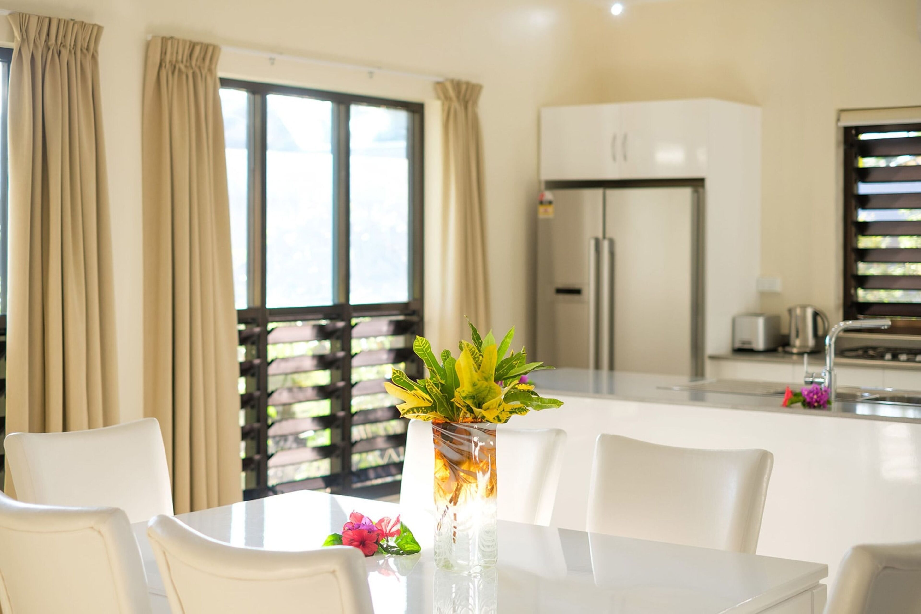 A modern kitchen with white cabinets, a stainless steel refrigerator, and a dining area with a white table and chairs.