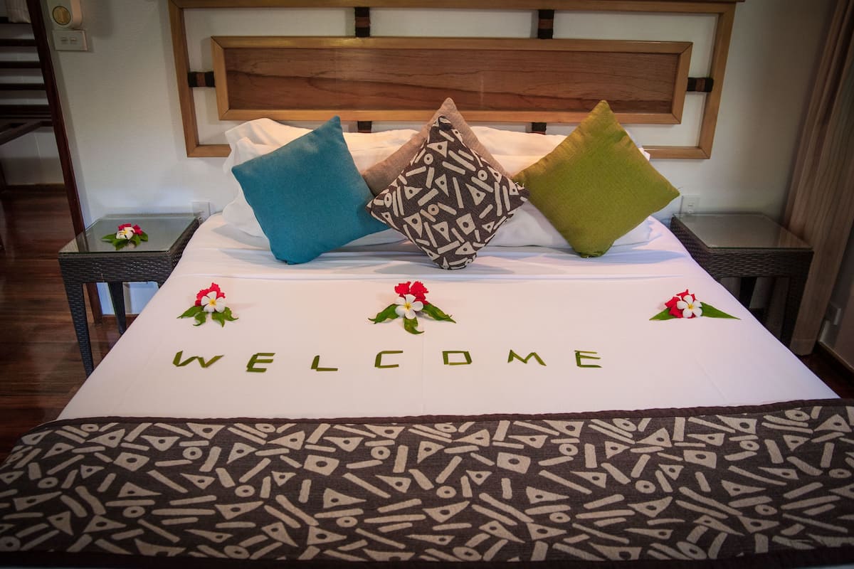 A neatly made bed with a 'WELCOME' sign, pillows, and flower arrangements.