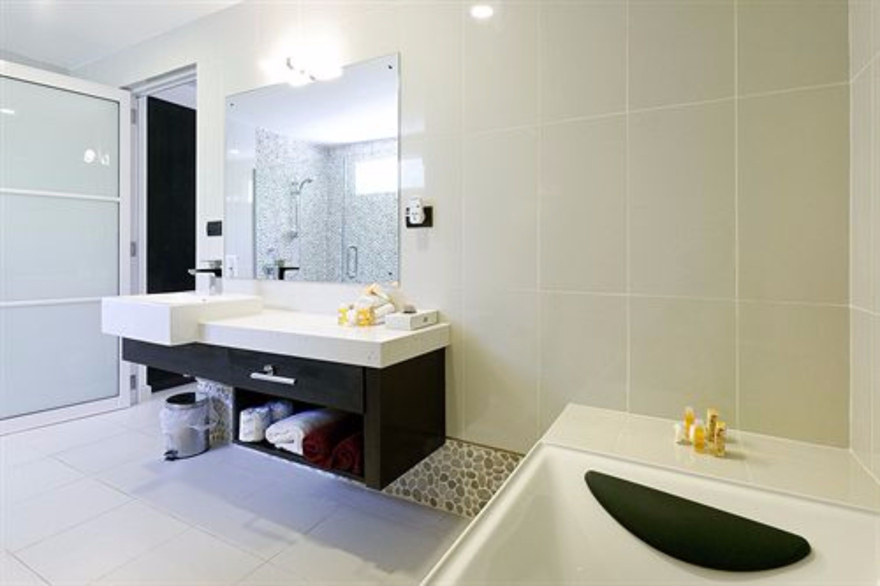 A modern bathroom with a white sink, dark cabinet, and a large mirror.