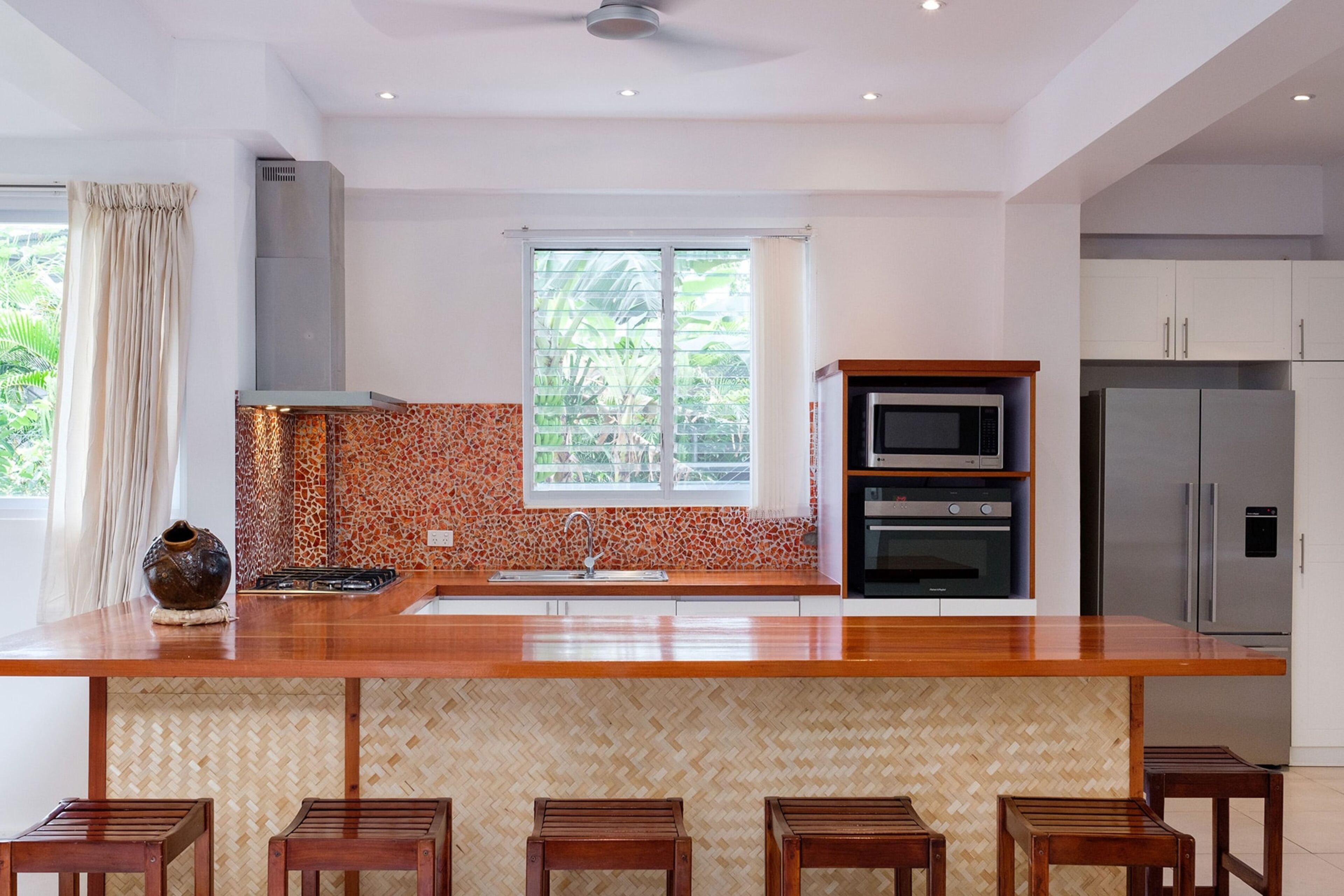 A modern kitchen with a large island, built-in oven, stainless steel appliances, and a herringbone-patterned backsplash.