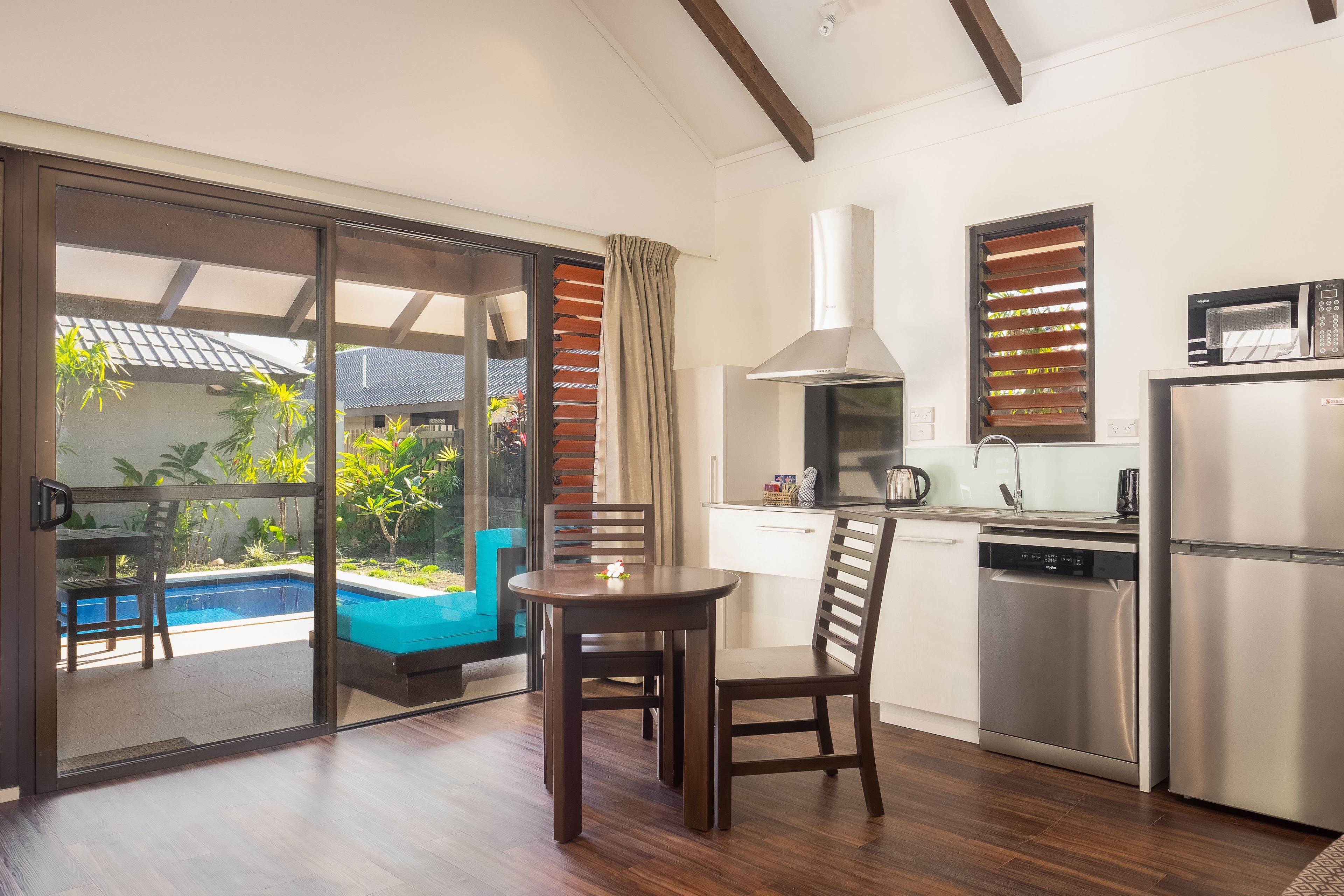 A modern kitchen with a dining area, a view of a swimming pool, and a sliding glass door leading to an outdoor seating area.