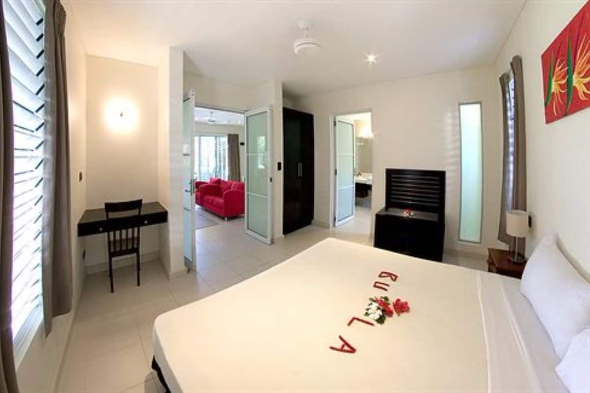 A hotel room with a bed, a desk, a chair, a red sofa, and a door leading to another room.