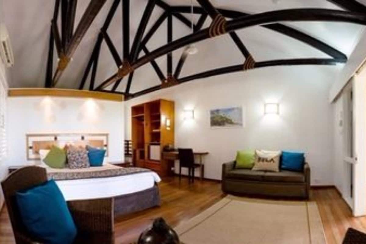A room with a high ceiling, exposed beams, a bed, a sofa, and a dining area.