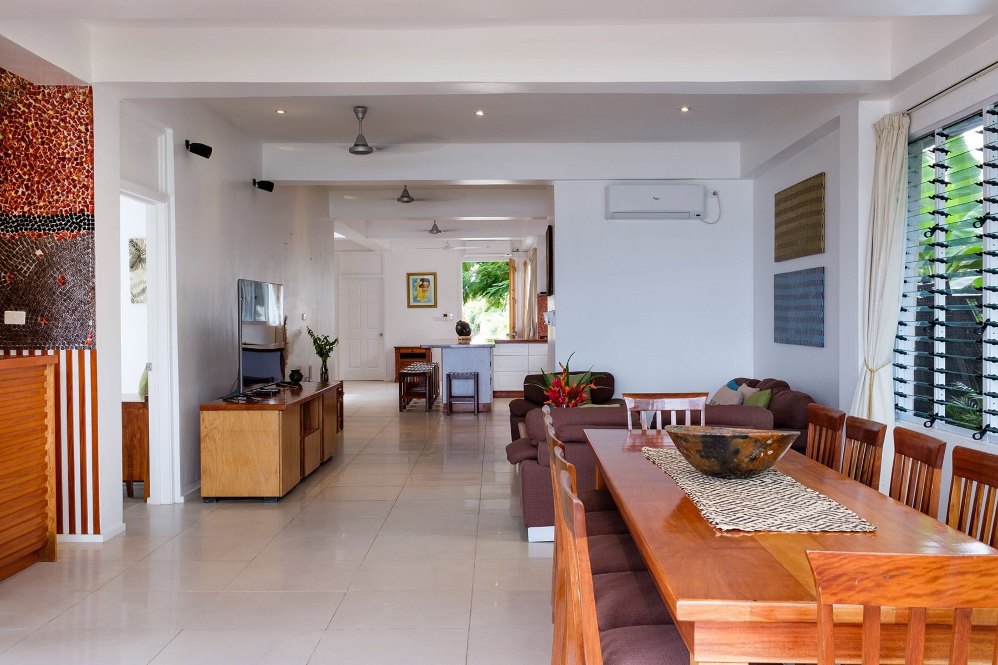 A spacious living area with a wooden dining table, a sofa, and a kitchen in the background.
