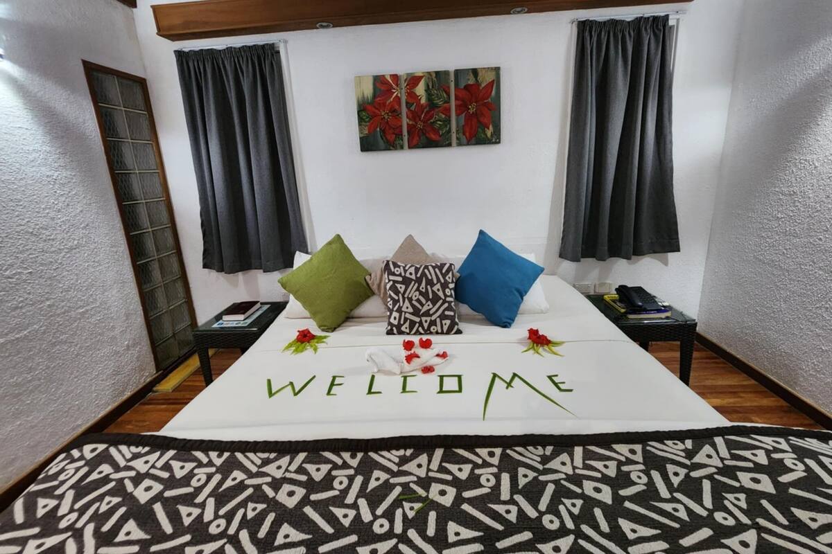 A cozy bedroom with a bed, a 'WELCOME' sign, and a painting of red flowers on the wall.