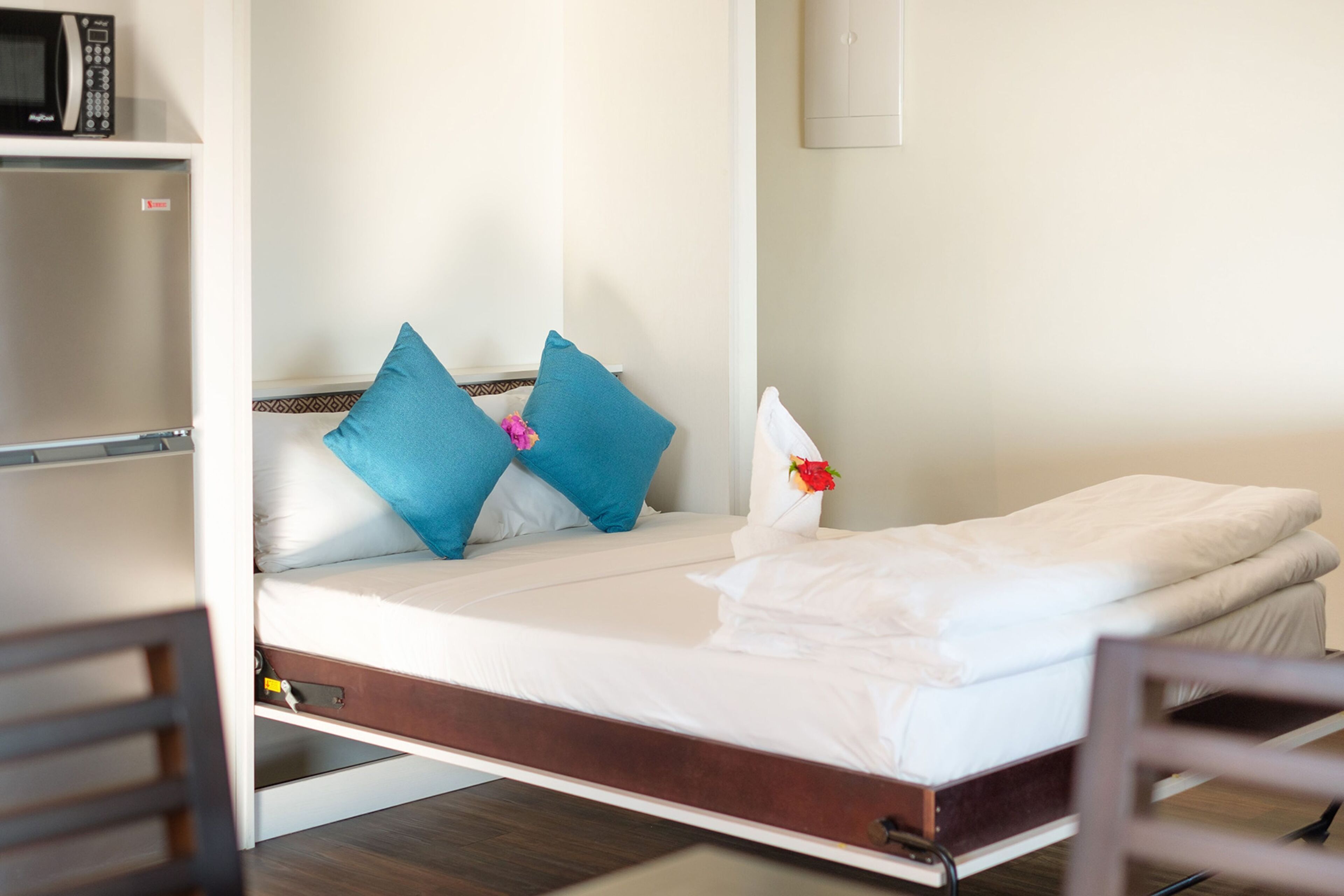 A single bed with a wooden frame, white bedding, and two blue pillows.