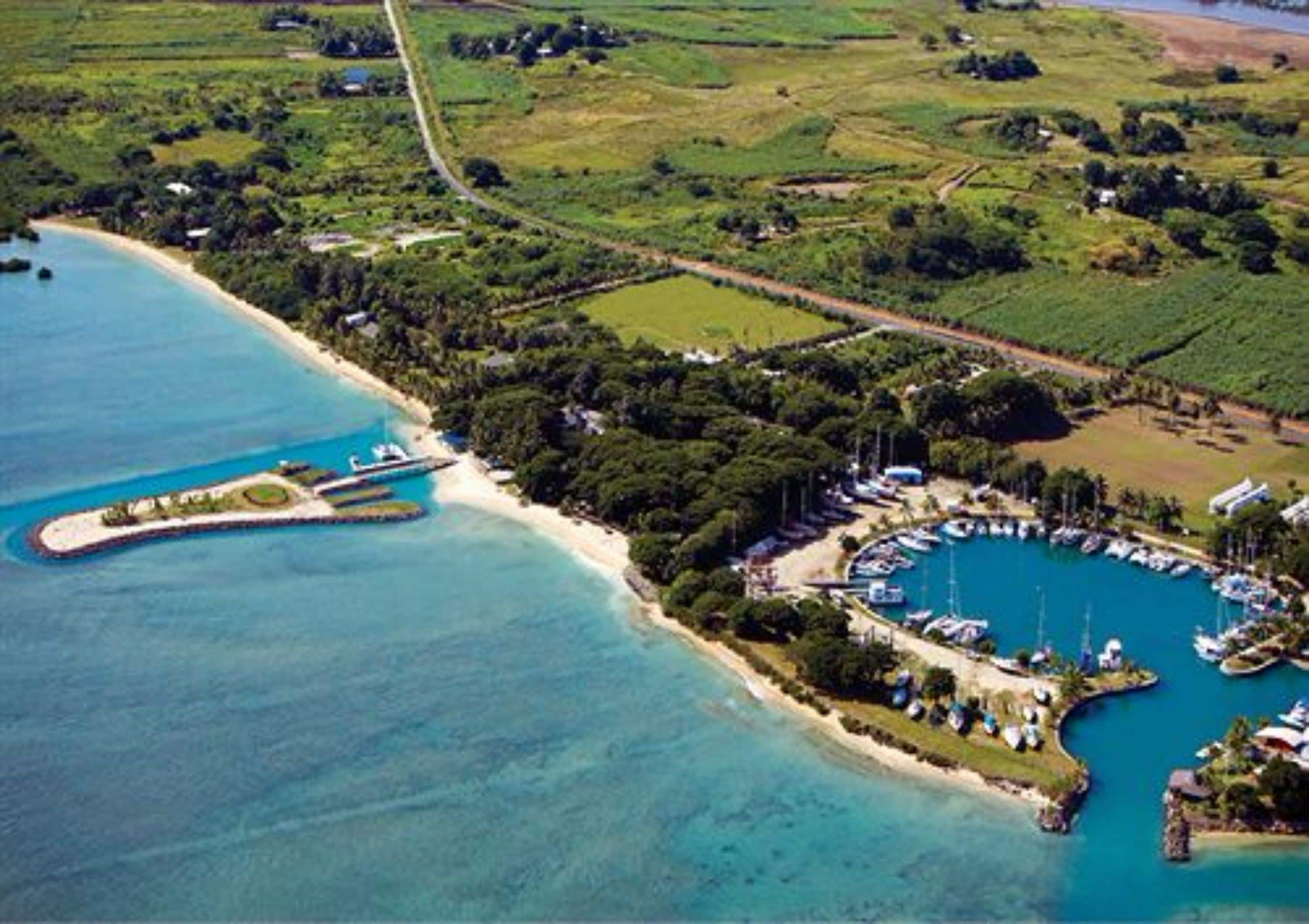 An aerial view of a coastal area with a marina, boats, and a small island with buildings.