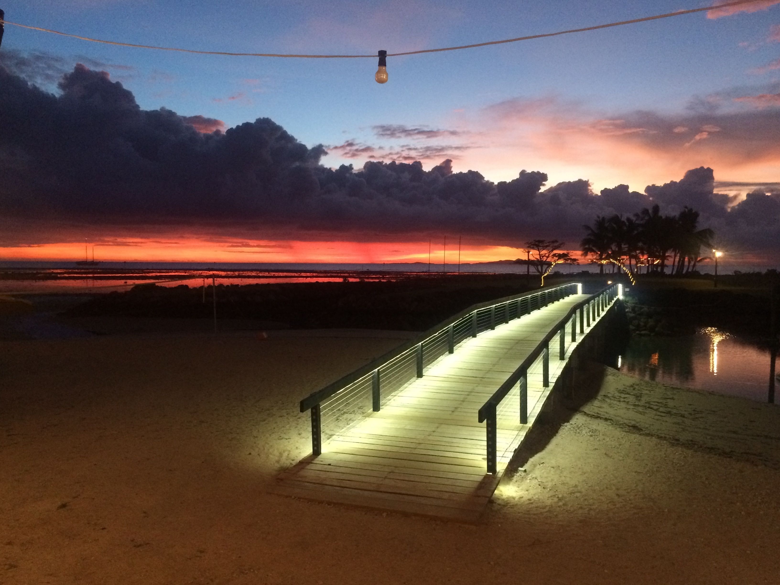 Un paseo marítimo de madera con barandillas que conduce a una playa al atardecer.