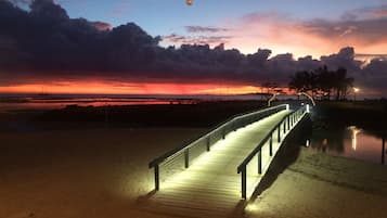 Un paseo marítimo de madera con barandillas que conduce a una playa al atardecer.