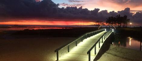 Un paseo marítimo de madera con barandillas que conduce a una playa al atardecer.