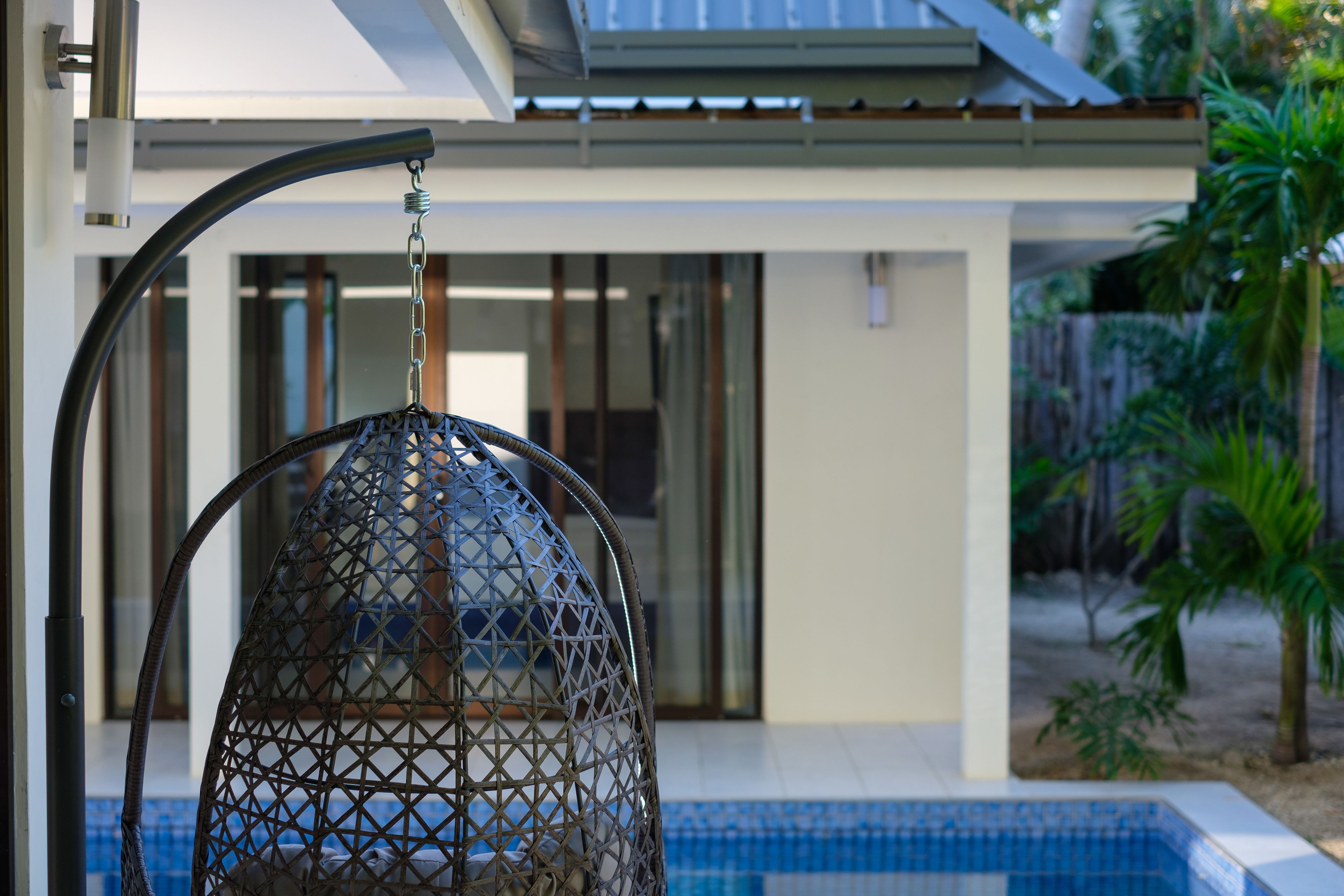 A hanging chair near a pool with a modern house in the background.