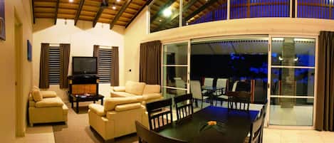A spacious living area with a high ceiling, a fireplace, and a dining table with chairs.