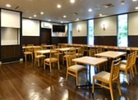 Un ristorante con tavoli e sedie in legno, luci a incasso nel soffitto e ampie finestre.